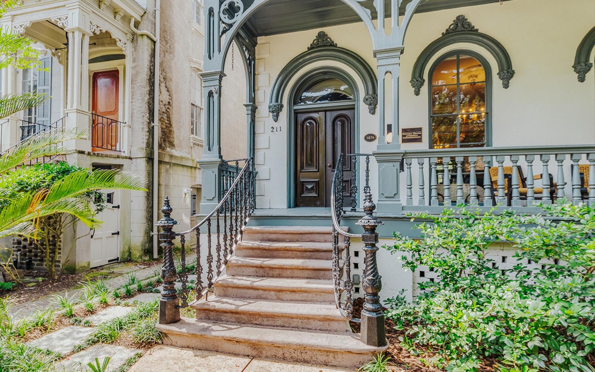 A Victorian-style house with ornate wooden trim, brick steps leading to a dark wooden door, and potted plants around the entrance area.