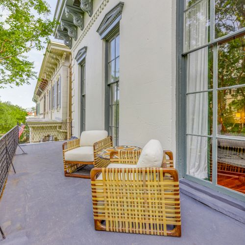 The image shows a balcony with two wicker chairs and a small table, overlooking a scenic view with trees and a neighboring building, ending the sentence.