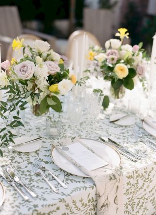 A beautifully set table adorned with floral arrangements, white plates, cutlery, menus, and glassware on a patterned tablecloth.